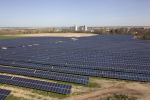 La centrale solaire de Bétheniville, dans la Marne (photo mise à disposition par le groupe Quadran Energies Libres). À droite, le site de Pantegnies, à Pont-sur-Sambre et à l’arrière-plan, dans la vapeur, l’ex-centrale Poweo rachetée par le fonds d’investissement américain KKR.